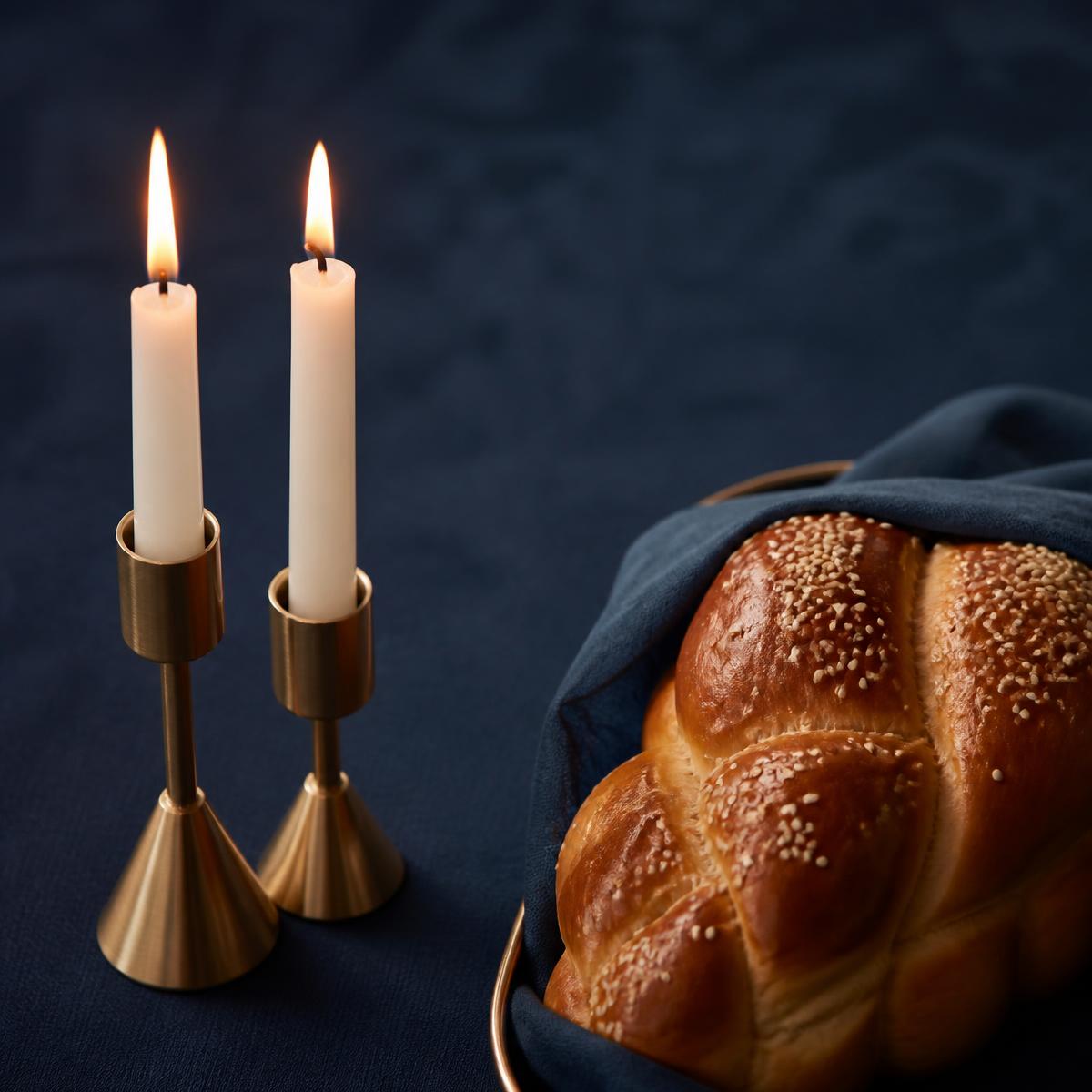 Two lit Shabbat candles beside a braided challah on a navy tablecloth