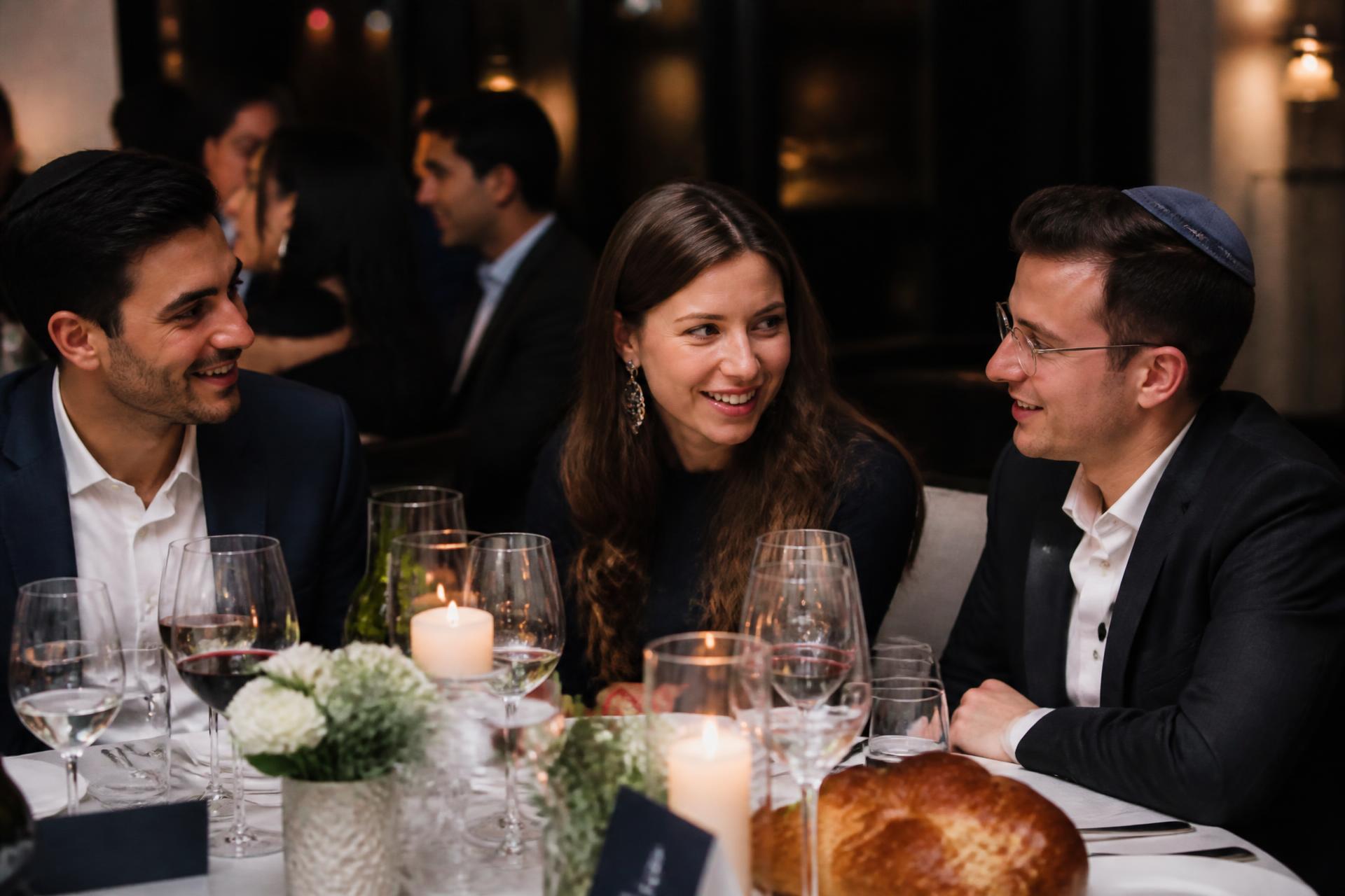 Young Jewish professionals in conversation at an elegant Shabbat dinner table with candles and challah
